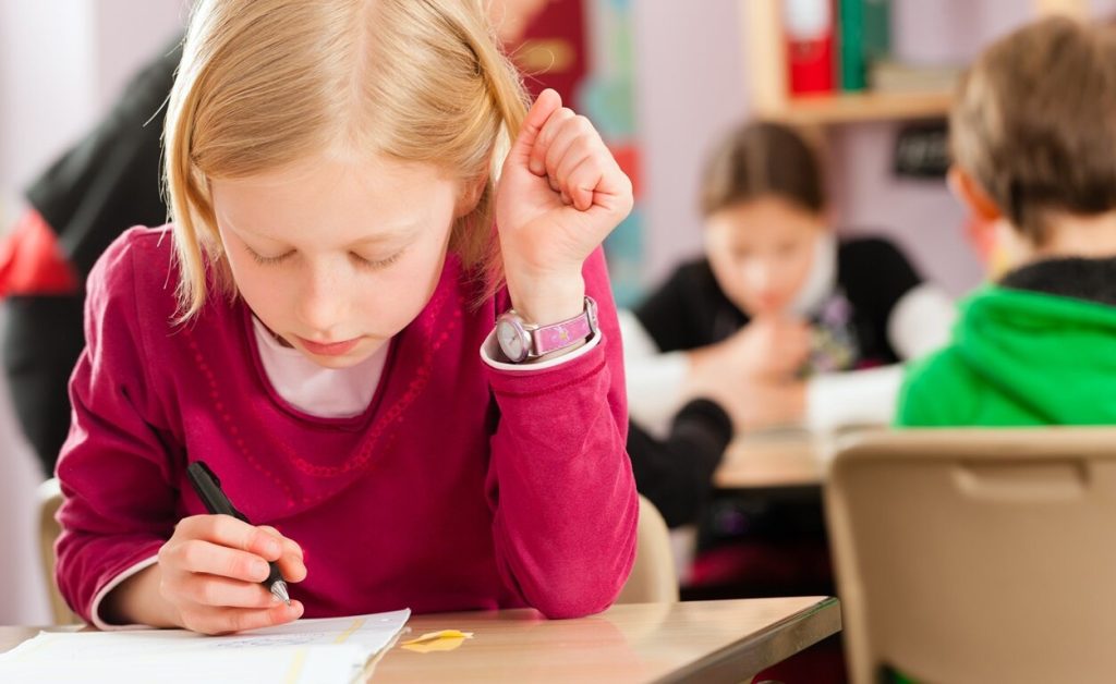 Child writing at a desk in a classroom.