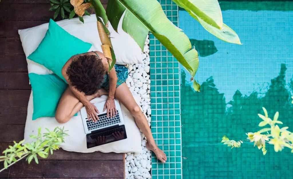 A person working remotely on a laptop in a tropical or poolside setting.
