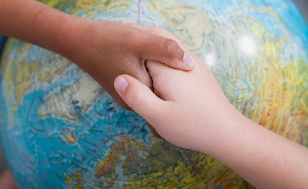 Hands holding together over a map of the world.