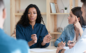 Woman sitting at a conference table, talking to a team of diverse professionals