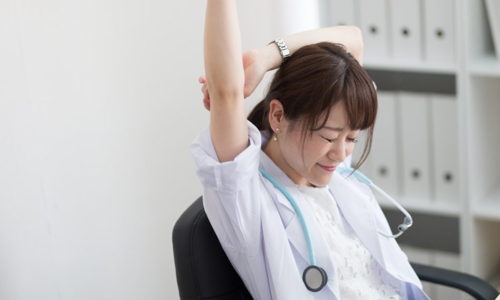 Young Asian nurse sitting and stretching her right arm in the air