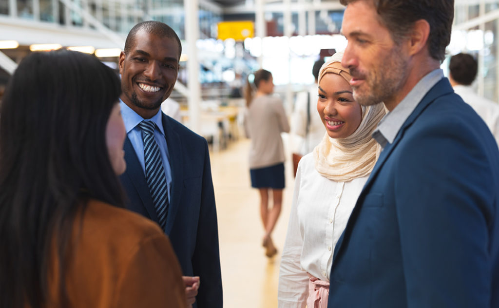 A diverse group of professionals stand in conversation, smiling and listening