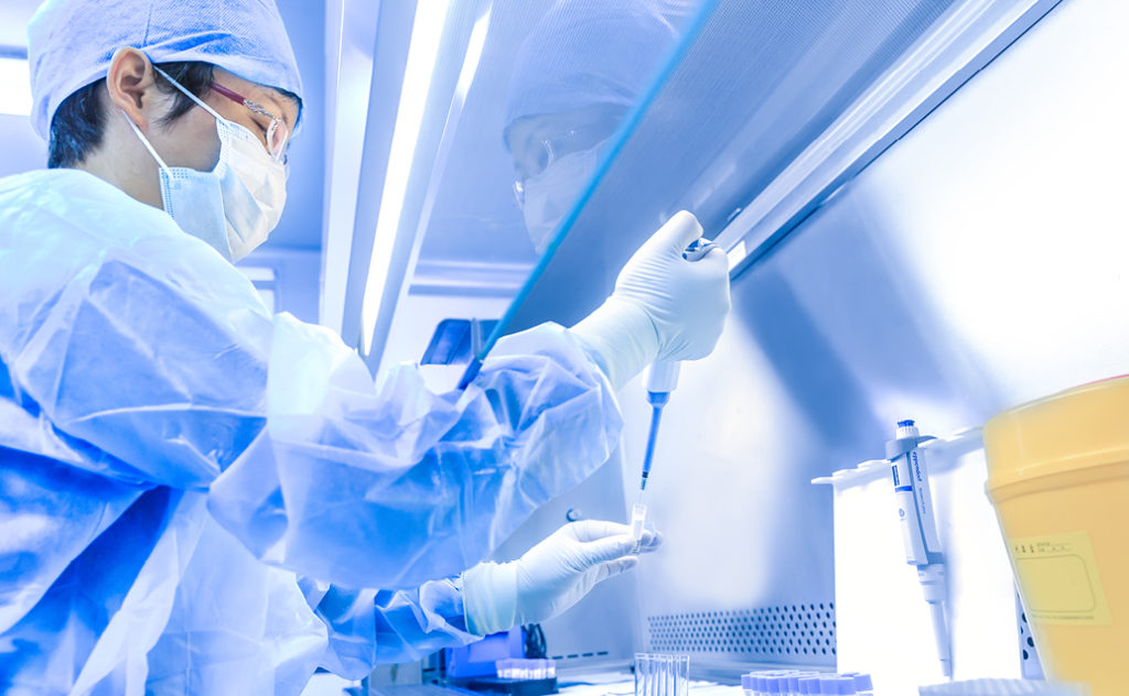 Asian male in protective lab gear uses a dropper to insert liquid into a test tube