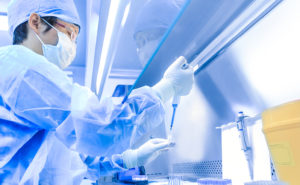 Asian male in protective lab gear uses a dropper to insert liquid into a test tube