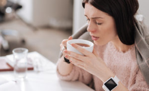 White woman with a blanket draped over her shoulders, about to drink a cup of tea as an alternative treatment