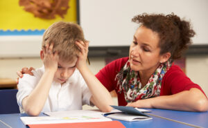 Photo of a female educator crouched next to a student holding his head in his hands in frustration