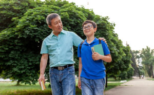 Photo of parent with child carrying backpack and homework