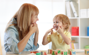 Woman and young child practicing mouth movements together at a table with alphabet blocks