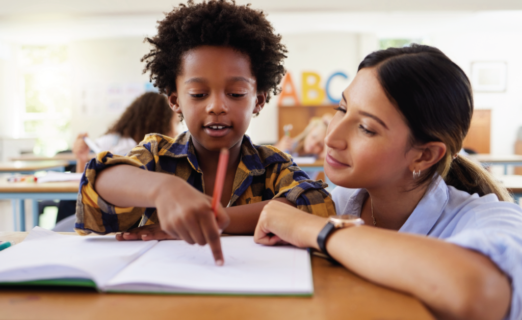 Teacher helping a student write in a classroom